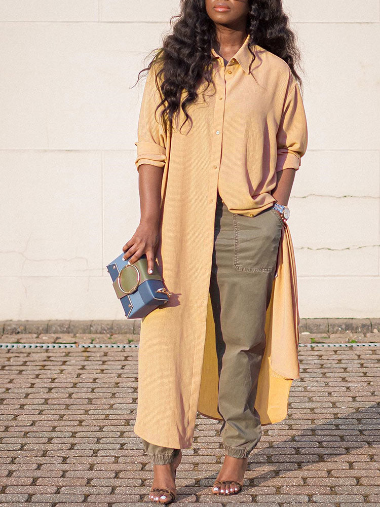 Woman wearing a long yellow collared shirt dress over olive green cargo pants and heels, holding a blue and green clutch.
