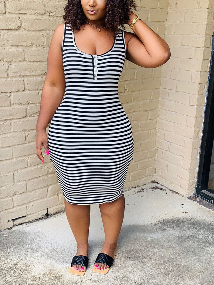 Woman wearing a black and white striped sleeveless dress with a scoop neckline and button detail, wearing black slides.