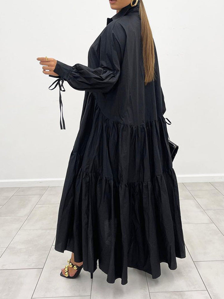 Woman wearing a black tiered maxi dress with long balloon sleeves, standing indoors and gesturing.