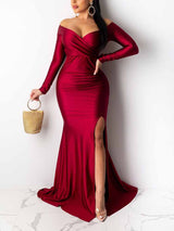 Woman in a long, off-the-shoulder, red satin dress with a high slit, holding a gold handbag.
