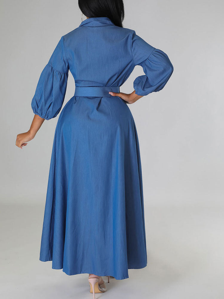 Woman posing from the back in a blue denim maxi dress with puffed sleeves and a belted waist.