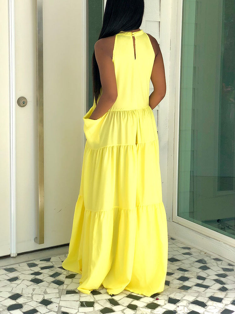 Back view of a woman in a yellow tiered maxi dress with a halter neckline and pockets.