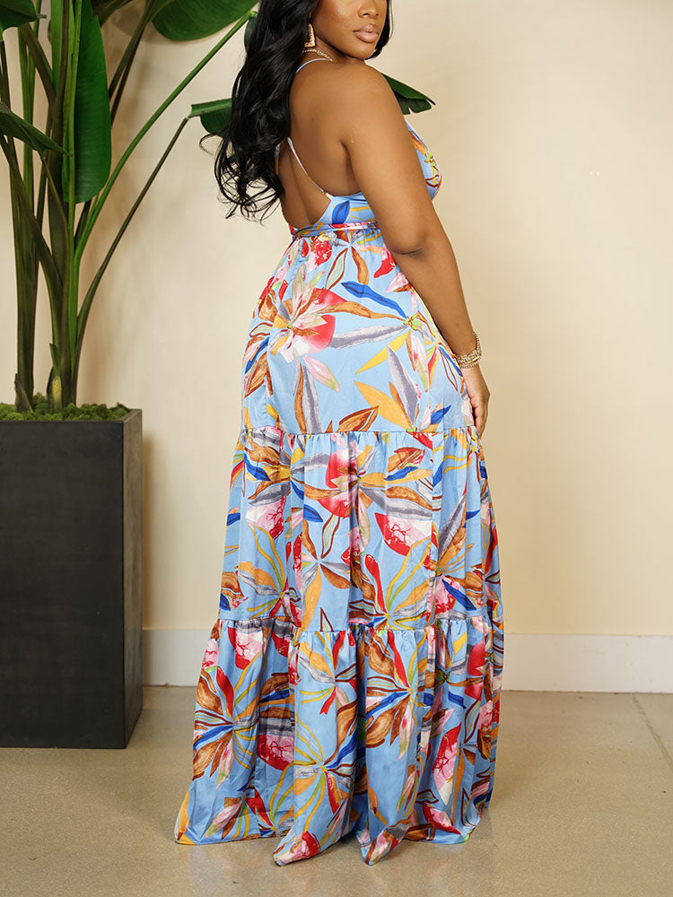 Back view of a woman wearing a light blue maxi dress with a tropical floral print, showcasing the tiered skirt and criss-cross back straps.