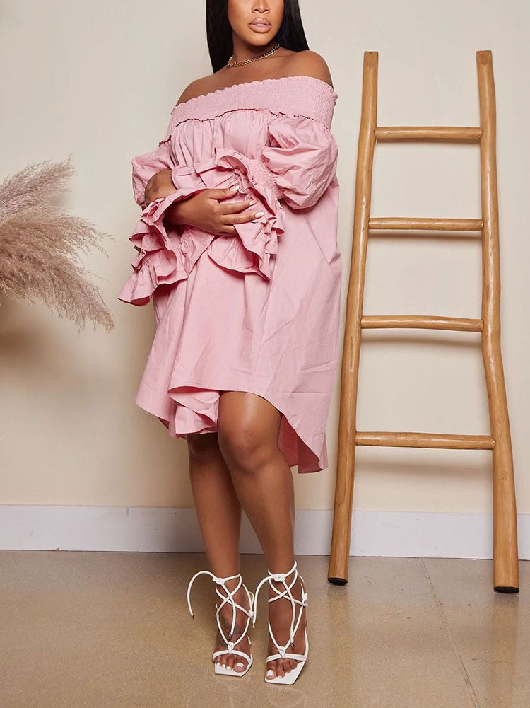 Woman wearing a light pink off-the-shoulder dress with tiered ruffled sleeves and a high-low hemline, holding her arms across her chest and paired with white strappy heels.