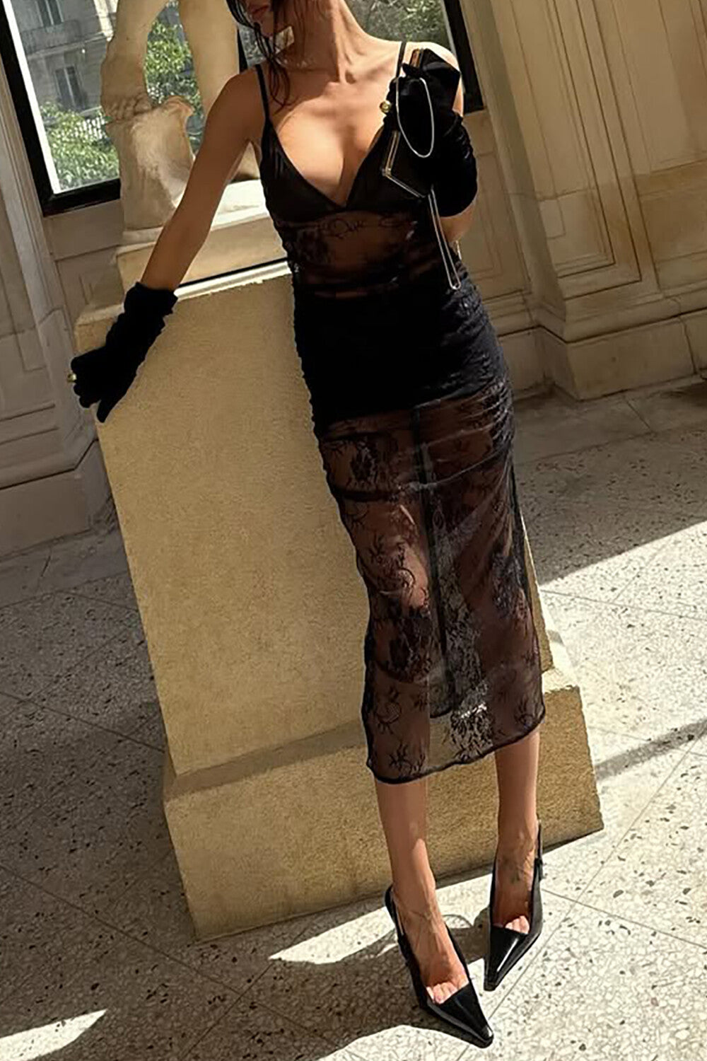 A woman in a black lace dress and gloves leans against a pillar.
