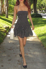 Woman in a black and white polka dot halter dress and black ballet flats, holding a white handbag.