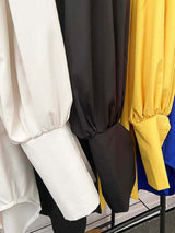 Close-up of the voluminous sleeves of shirt dresses in beige, black, and yellow.