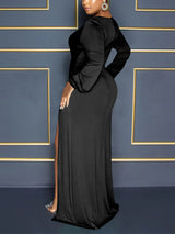 Side view of a woman wearing a black long-sleeve maxi dress with a deep V-neckline and a high slit.