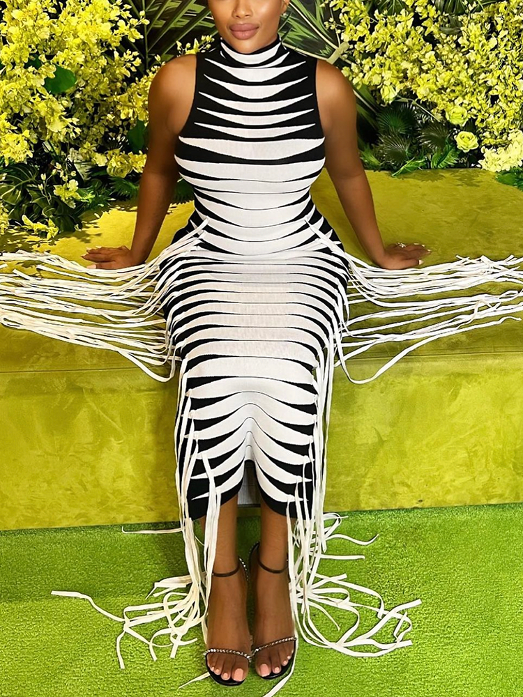 Woman wearing a black and white striped knit dress with fringe, seated on a green bench with yellow flowers.