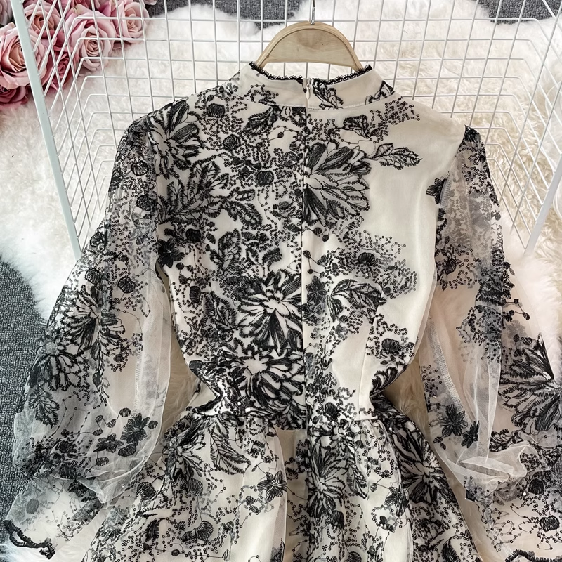 Detail shot of the sequin and lace trim on the mock neck of a black and white floral embroidered midi dress.