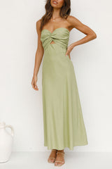 woman with hand on hip in a light green strapless satin dress with a twisted bust and cut-out waist, standing against a white wall