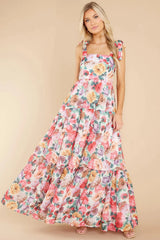 Model posing in a long floral dress with a square neckline and tie shoulder details.