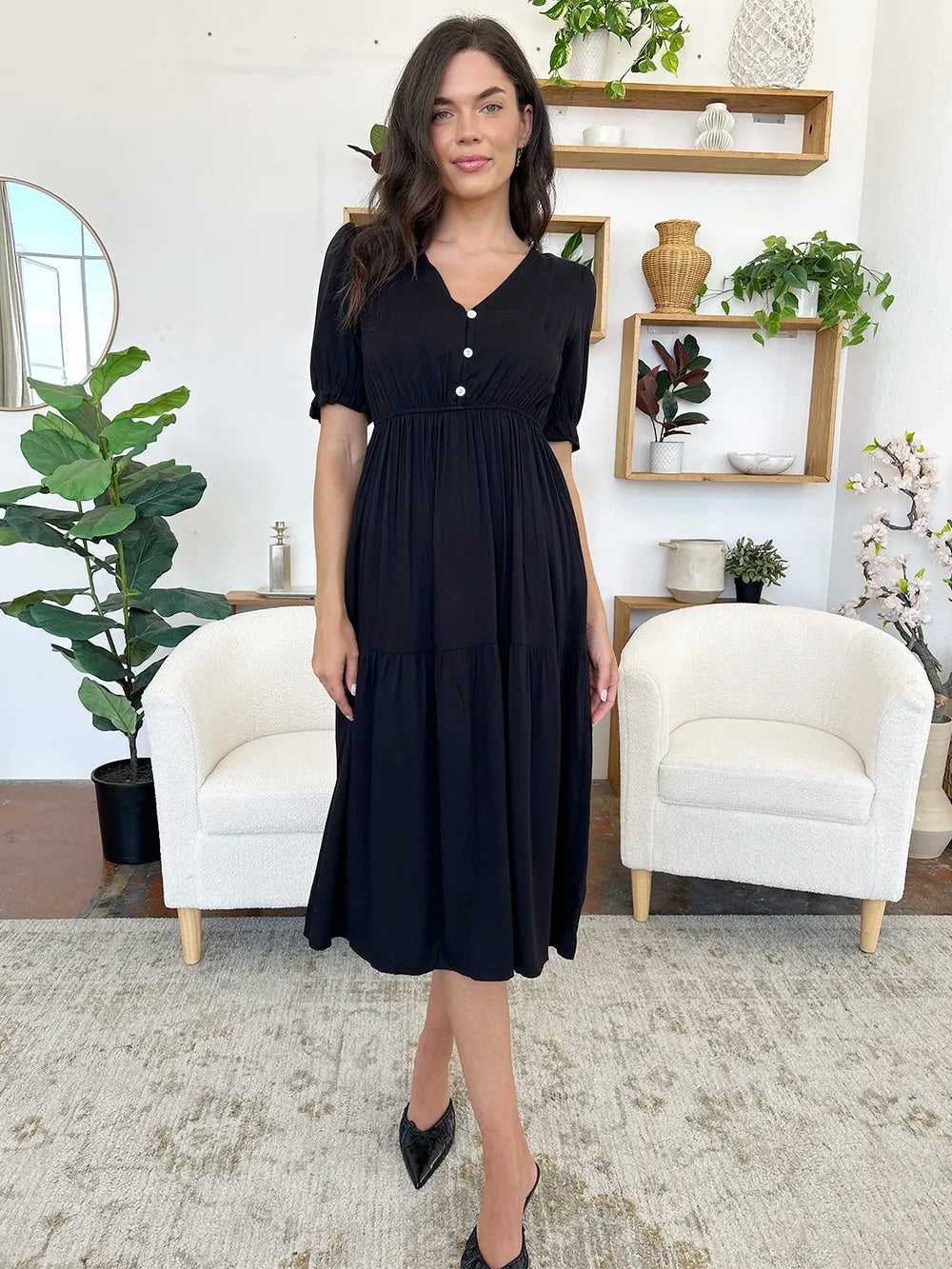 Full body shot of a woman wearing a black midi dress with short sleeves and a tiered skirt.