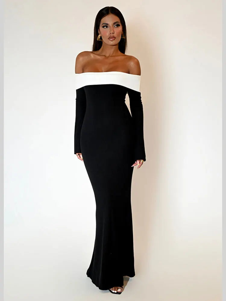Woman wearing a black off-the-shoulder floor-length dress with a white trim, standing against a white background.