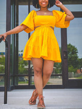 Woman wearing a yellow two-piece set with a square neckline, puff sleeves, and a tiered skirt.