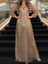 Woman in a long, sheer, sparkling gold dress with long sleeves and a V-neck, standing on stairs.