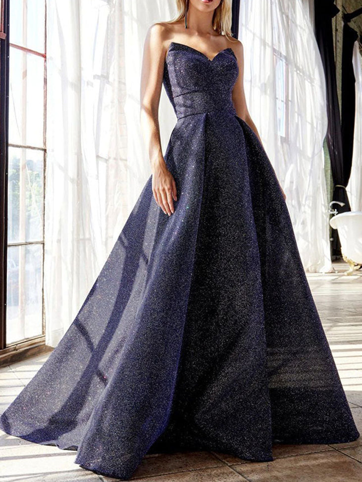 Model wearing a navy blue sparkly strapless ball gown with a full skirt, standing near a window.