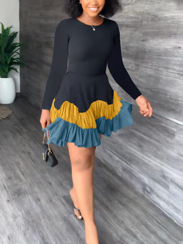 Woman wearing a black long-sleeved dress with a tiered, ruffled hem in shades of yellow and blue.