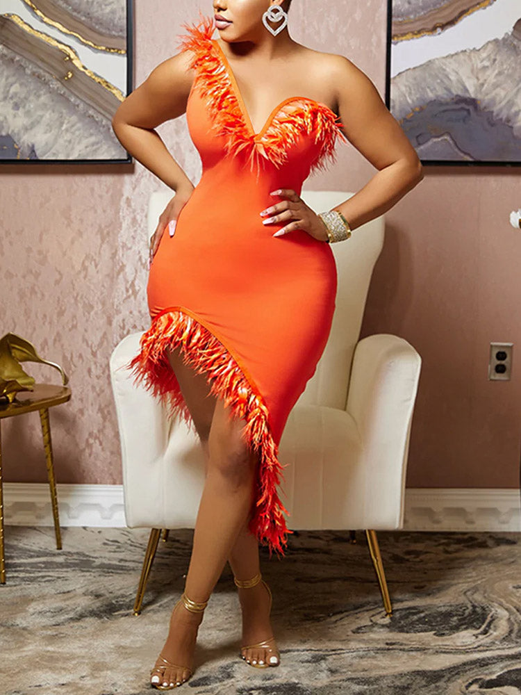 Woman wearing an orange one-shoulder dress with feather trim and asymmetrical hemline, standing next to a white armchair.