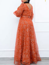 Rear view of a woman wearing a long orange floral print gown with sheer puff sleeves and a V-neckline.