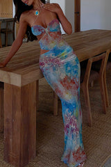 Full-length view of a woman wearing a vibrant, sheer maxi dress with a halter neckline and cut-out details.