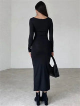 Back view of a woman wearing a long-sleeved, ruched, black maxi dress and black ankle boots.