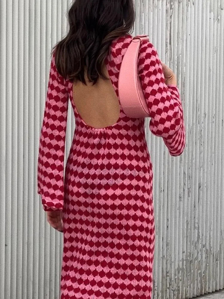 Woman from behind wearing a long-sleeved knit dress with an open back and a pink and red geometric diamond pattern, carrying a pink shoulder bag.