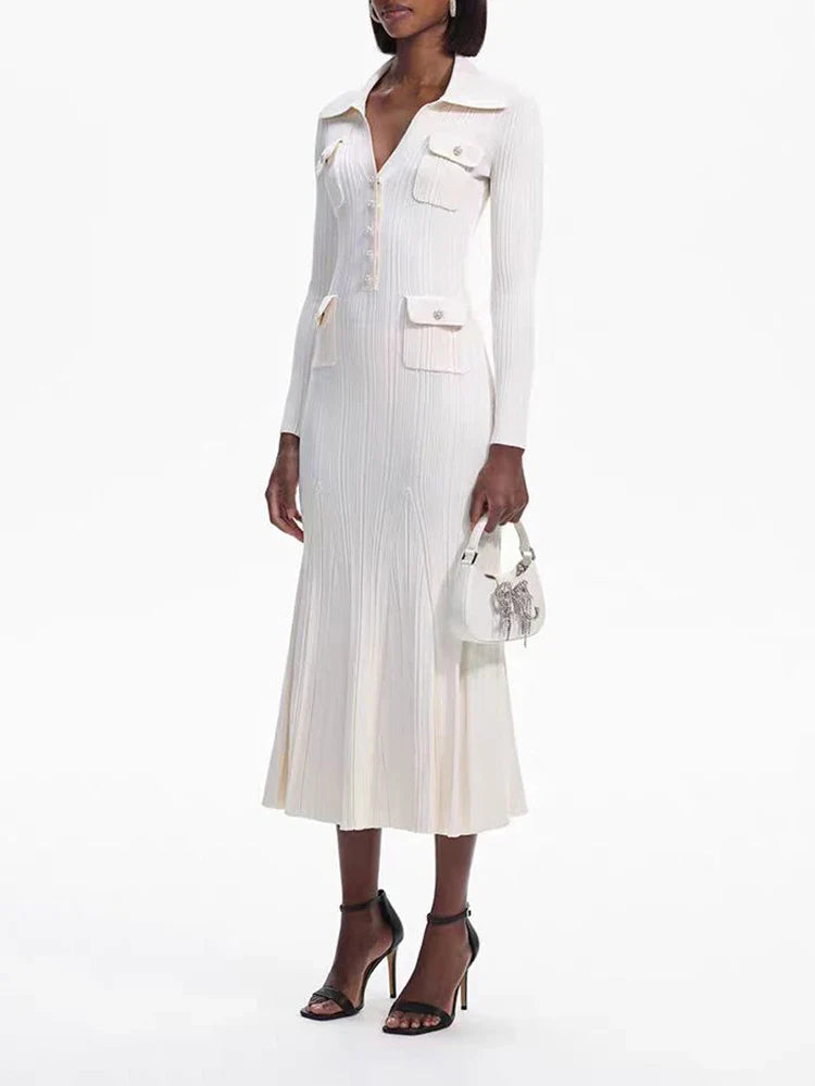 Woman wearing a cream-colored long-sleeved knit dress with a collared neckline, button-up front, dual chest pockets, and a flared hem, holding a white handbag and wearing black heels.