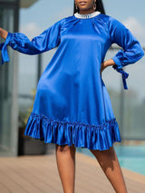Side view of a woman in a royal blue satin dress with bell sleeves tied with bows and a ruffled hem.