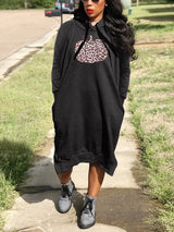 Woman wearing a black hooded midi dress with a pumpkin graphic print and leopard pattern, standing outdoors.