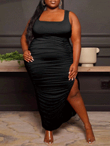 woman wearing a black ruched midi dress with a square neckline and high slit, showing the side view