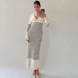 Woman wearing a long-sleeved striped maxi dress and white heels, taking a mirror selfie