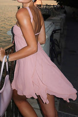 woman wearing a pink halter dress with ruffled hem standing near a railing by the water