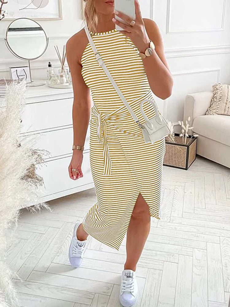 Full body shot of a woman in a yellow and white striped halter neck dress with a tie waist and side slit, accessorized with white sneakers and a white crossbody bag.