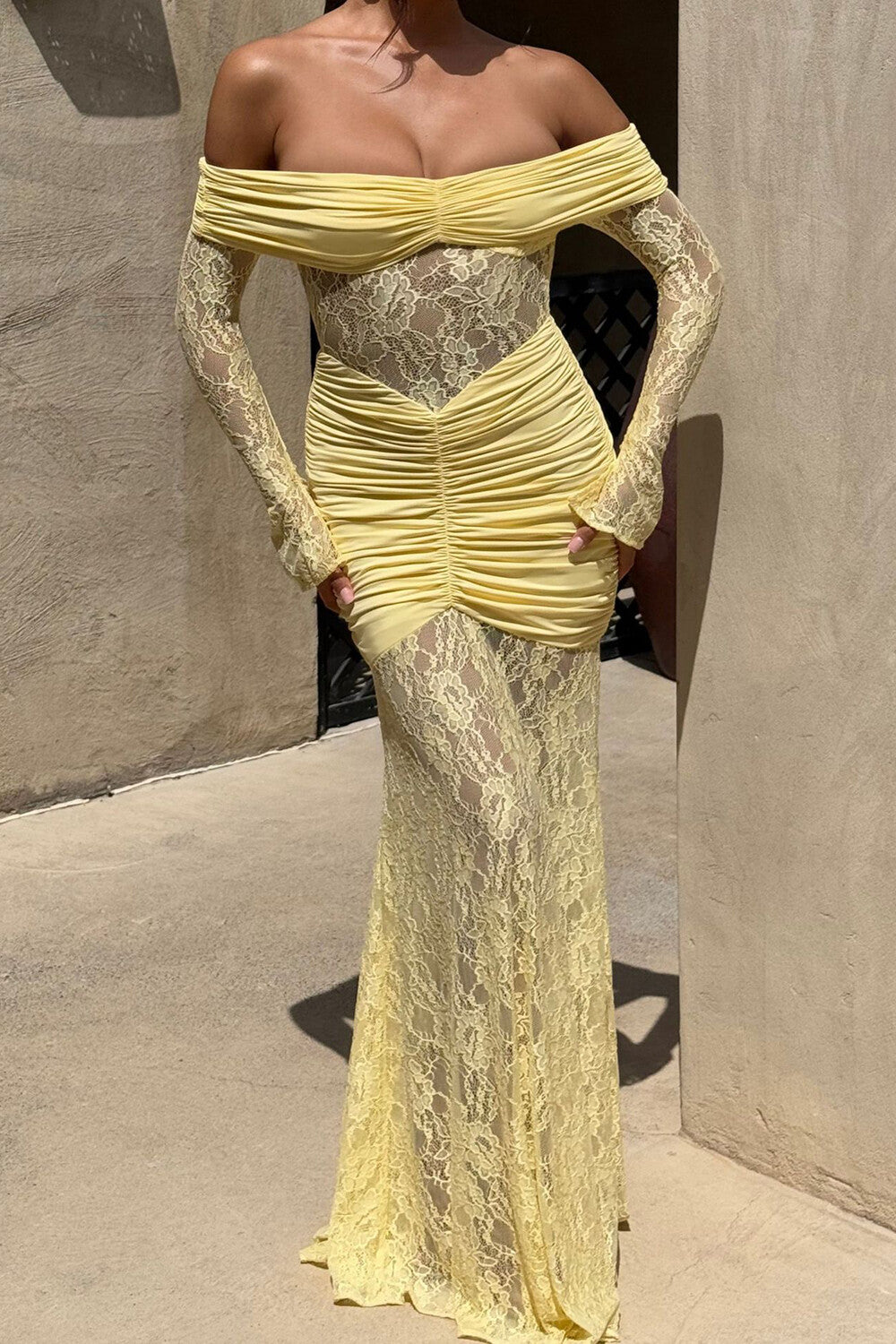 Woman wearing a pale yellow off-the-shoulder formal dress with long lace sleeves and ruched detailing.