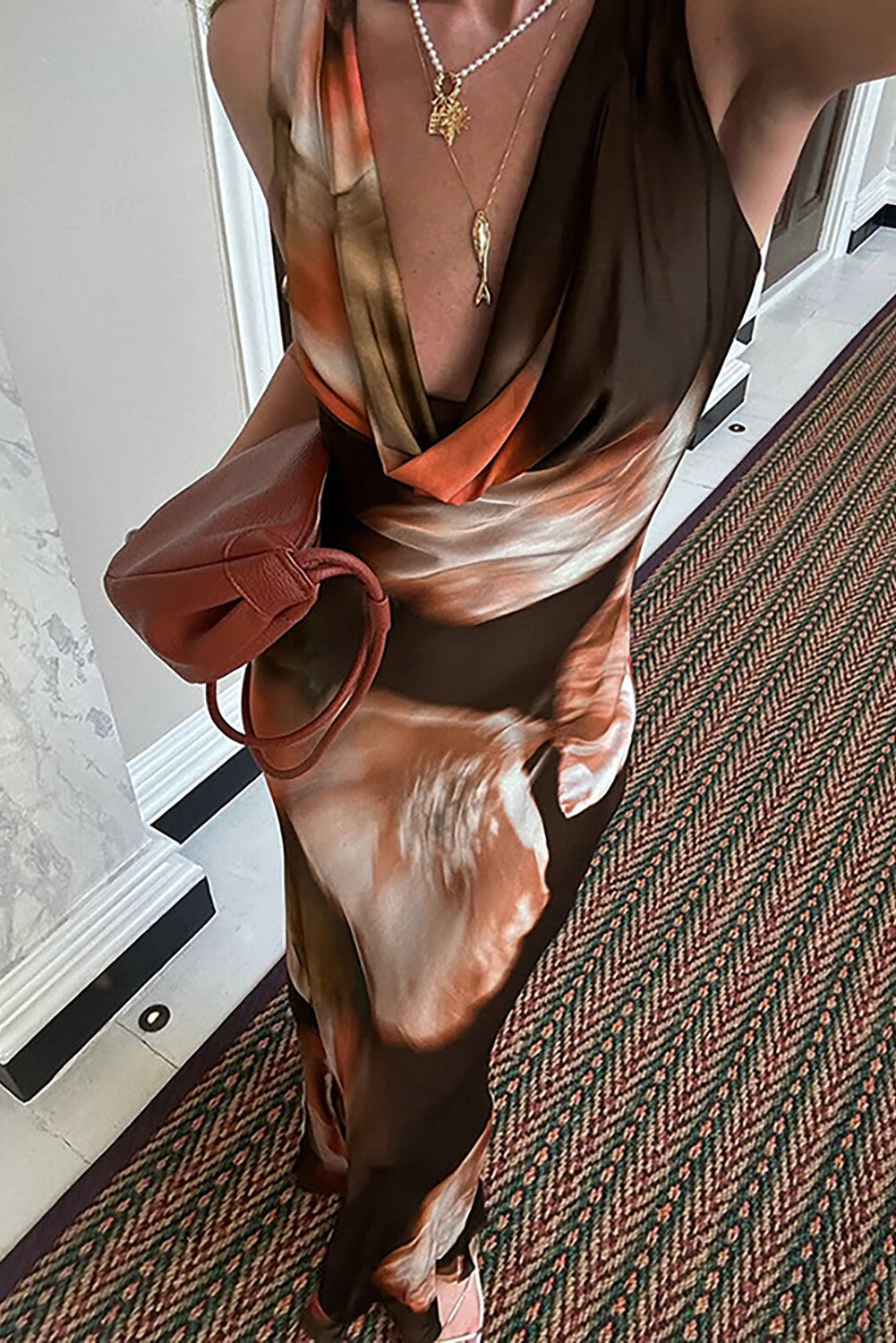 Close-up of a woman wearing a long, draped dress with a brown, orange, and white abstract print and a gold pendant necklace.