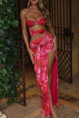 Full body shot of a woman in a red abstract print halter top and matching maxi skirt with a high slit.