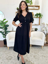 Woman in a black midi dress with short sleeves, smiling and posing with her hand on her hip.