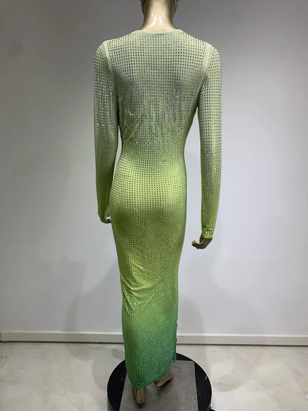 Back view of a mannequin wearing a long, gradient green rhinestone-embellished dress with long sleeves.