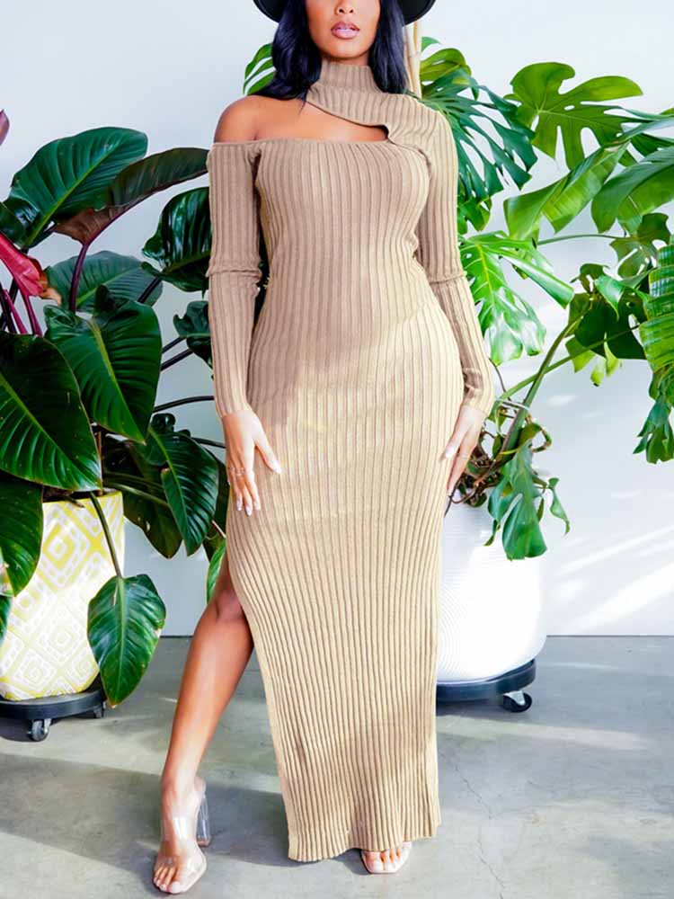Woman wearing a beige ribbed knit maxi dress with a high slit and asymmetrical shoulder cut-out, standing in front of large green plants.