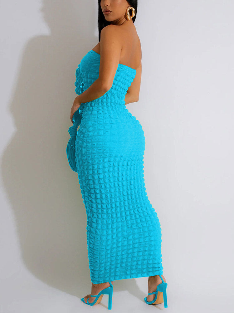 Woman from the back wearing a strapless blue midi dress with textured fabric and ruched detailing at the bust, holding a blue clutch bag and wearing blue strappy heels.