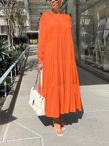 Woman wearing a long, orange tiered maxi dress with long sleeves and a white handbag.