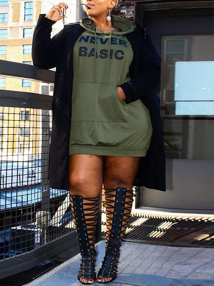 Plus-size model wearing a green hooded dress with 'Never Basic' graphic, black coat, and lace-up boots.