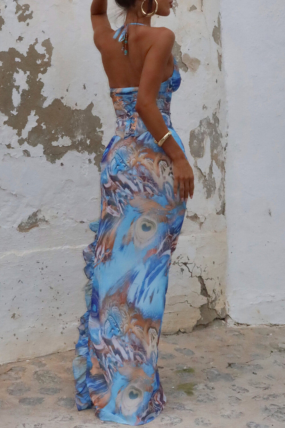 Rear view of a woman wearing a blue abstract print sheer mesh maxi dress with a high slit and halter neckline.