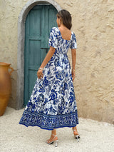 Back view of a woman wearing a blue and white floral print maxi dress with puff sleeves and a square neckline.