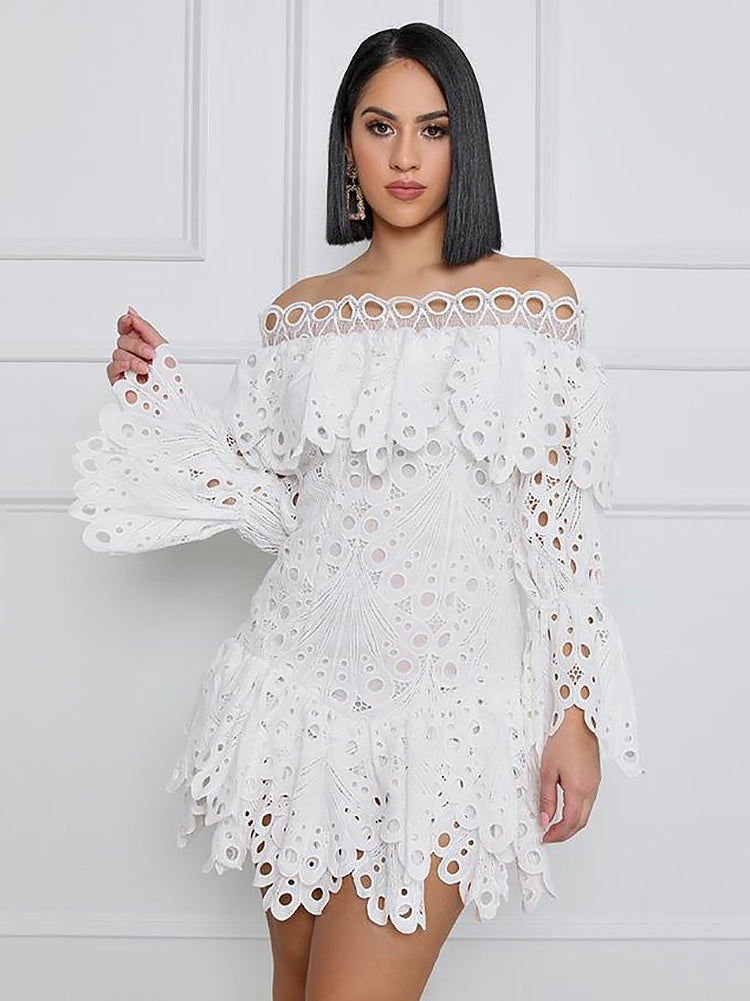 Woman wearing a white off-the-shoulder eyelet lace mini dress with bell sleeves and ruffled tiers, standing against a white wall.