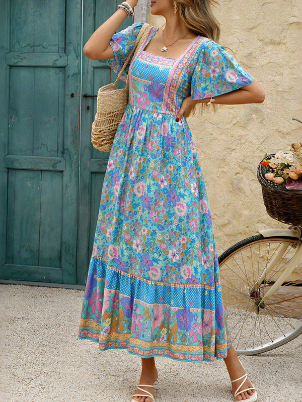 Woman wearing a blue floral print maxi dress with flutter sleeves and a square neckline, standing outdoors.