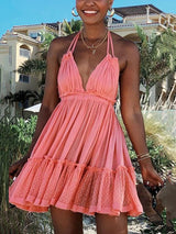 Woman wearing a coral pink halter neck mini dress with a deep V-neckline and tiered ruffled skirt, outdoors with palm trees and a building in the background.