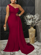 Woman wearing a burgundy one-shoulder formal gown with a thigh-high slit and mermaid hemline, holding a clutch.