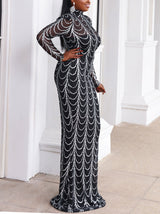 Side view of a woman in a long black dress with silver wavy embellishments, posing outdoors with white columns.